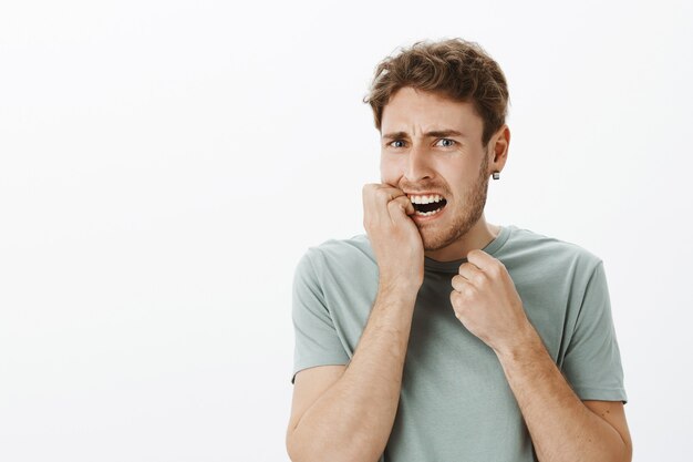 Portrait d'homme européen anxieux a souligné avec des cheveux blonds, se mordant l'ongle et fronçant les sourcils, grimaçant de peur, d'être nerveux et effrayé