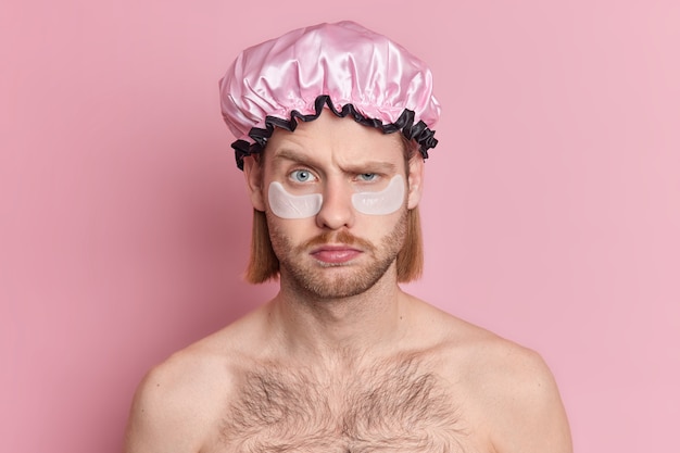 Portrait d'un homme européen mécontent soulève les sourcils regarde avec une expression grincheuse applique des patchs de collagène sous les yeux