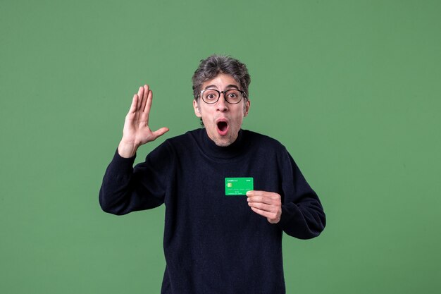 Portrait d'un homme de génie tenant une carte de crédit dans un mur vert tourné en studio