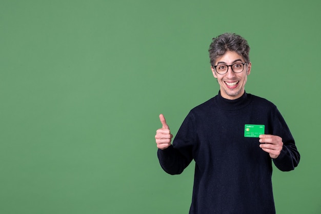 Portrait d'un homme de génie tenant une carte de crédit verte dans un mur vert tourné en studio