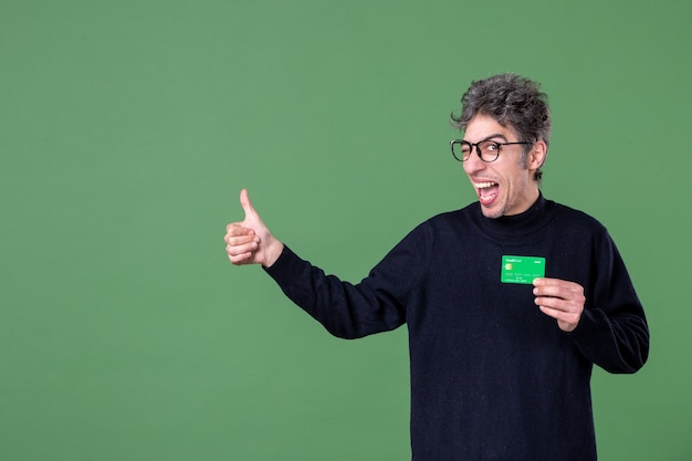 Portrait d'un homme de génie tenant une carte de crédit verte dans un mur vert tourné en studio