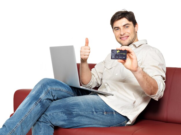 Portrait d'homme heureux souriant avec ordinateur portable donne les pouces vers le haut et montre la carte de crédit isolée sur blanc.