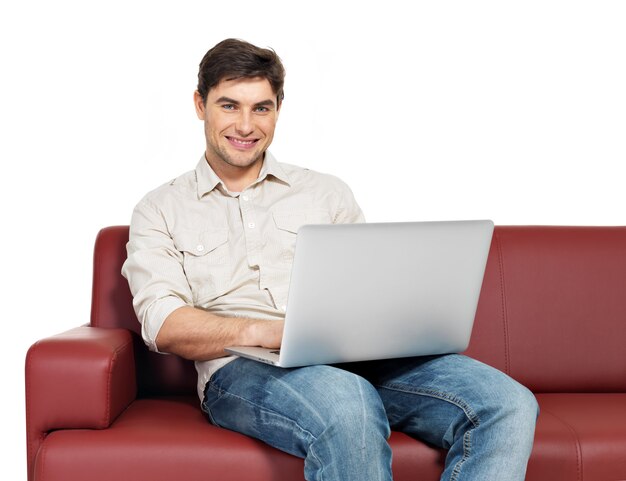 Portrait d'homme heureux souriant avec ordinateur portable est assis sur un divan, isolé sur blanc.