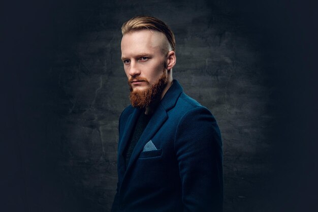 Portrait d'homme hipster barbu rousse vêtu d'une veste bleue sur fond gris.