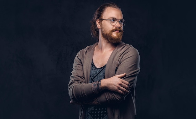 Portrait d'un homme hipster rousse vêtu de vêtements décontractés avec des lunettes et une barbe pleine, debout avec les bras croisés dans un studio. Isolé sur un fond sombre.