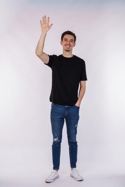 Portrait d'un homme joyeux et amical en t-shirt noir et jeans disant bonjour à la personne de bienvenue en agitant la main