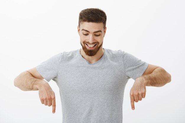 Portrait d'homme masculin heureux et étonné avec une coiffure et une barbe parfaites regardant et pointant vers le bas avec délice et curiosité en appréciant de regarder vers le bas à un espace de copie intéressant