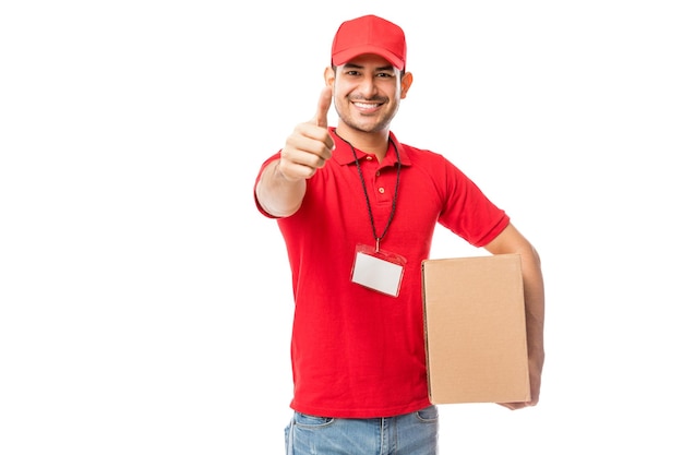 Portrait d'un homme de messagerie confiant avec boîte de déménagement montrant les pouces vers le haut sur fond blanc