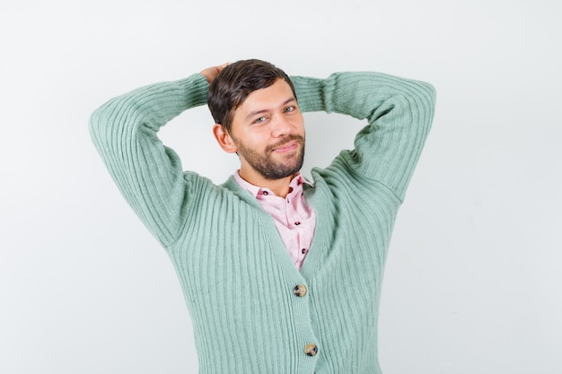 Portrait d'homme mûr avec les mains derrière la tête tout en posant en chemise, cardigan et à la vue de face heureuse