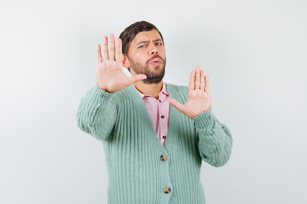 Portrait d'homme mûr montrant un geste d'arrêt en chemise, cardigan et regardant pensive vue de face