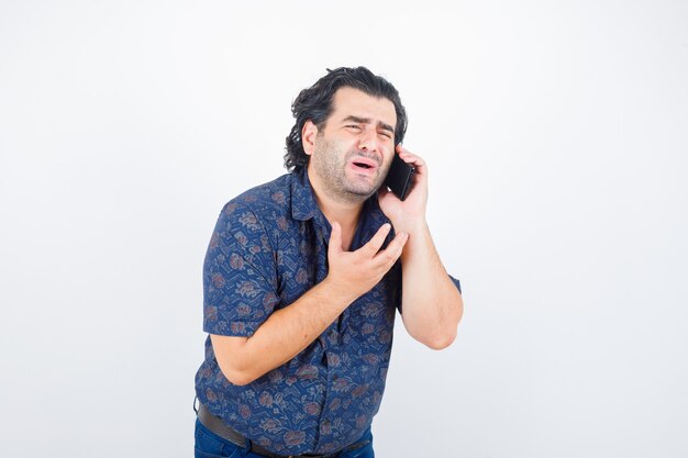 Portrait d'homme mûr parlant au téléphone mobile en chemise et à la vue de face nostalgique