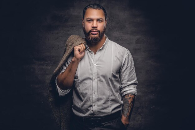 Portrait d'homme noir barbu avec bras tatoué portant une chemise blanche.