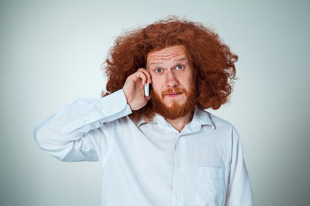 Portrait d'un homme perplexe parlant au téléphone un mur gris