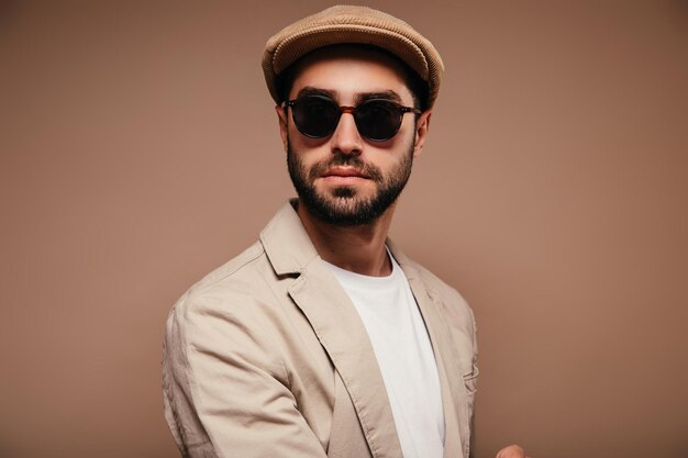 Portrait d'un homme portant une casquette de veste beige et des lunettes de soleil sur fond isolé