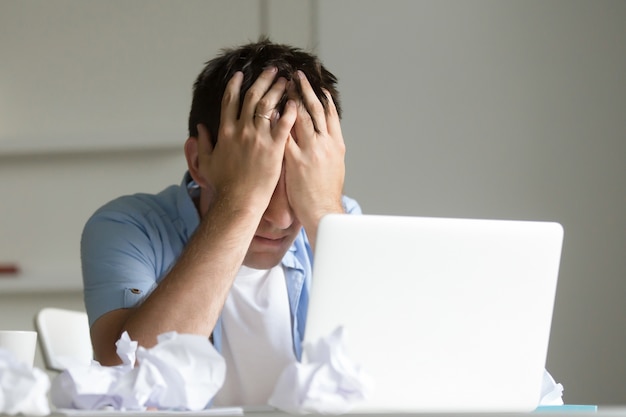 Portrait d&#39;un homme près de l&#39;ordinateur portable, ses mains fermant son visage