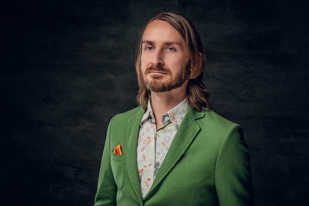 Portrait d'un homme réfléchi aux cheveux longs et au style rétro dans un studio photo sombre.