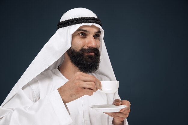 portrait de l'homme saoudien arabe. Jeune mannequin debout et buvant du café ou du thé.