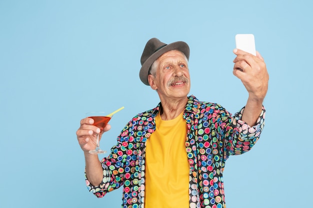Portrait d'homme senior hipster à l'aide d'appareils, gadgets isolés sur fond de studio lumineux. Concept de mode de vie des personnes âgées tech et joyeux.