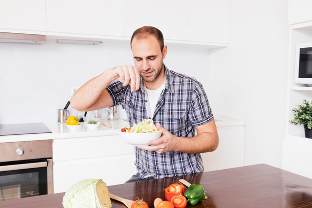 Portrait d&#39;un homme souriant, ajoutant des épices dans une salade