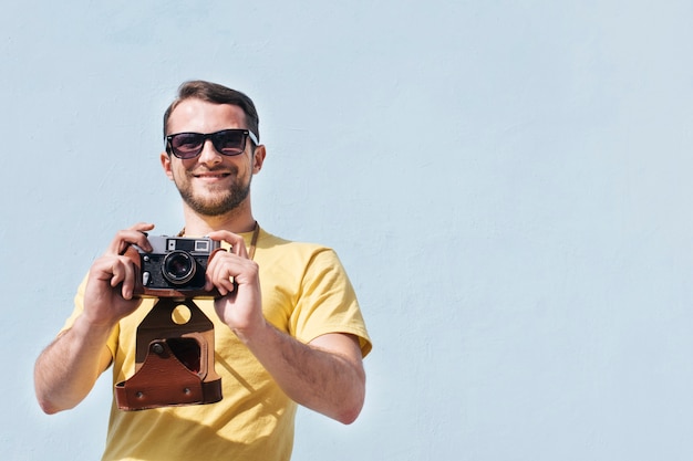 Portrait d'un homme souriant, lunettes de soleil prenant une photo avec l'appareil photo rétro