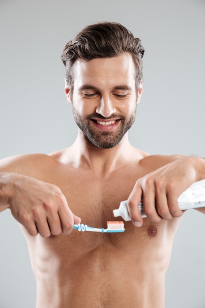 Portrait d'un homme souriant, mettre du dentifrice sur une brosse à dents