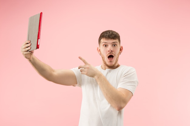 Portrait d'un homme souriant pointant sur un ordinateur portable avec écran blanc isolé sur fond rose de studio. Émotions humaines, concept d'expression faciale et concept publicitaire.