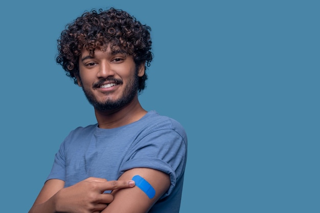 Portrait d'un homme souriant pointant son index vers le pansement adhésif sur le haut de son bras