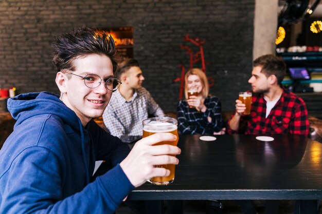 Portrait d&#39;un homme tenant le verre de bière assis avec des amis