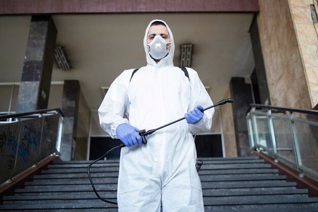 Portrait d'homme en tenue de protection blanche avec réservoir de pulvérisateur prêt pour une lutte contre le virus corona