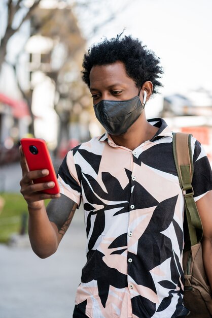 Portrait d'homme de tourisme afro à l'aide de son téléphone portable tout en marchant à l'extérieur dans la rue