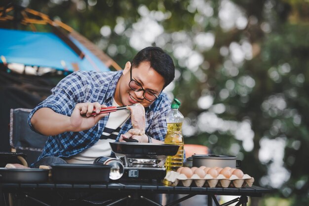 Photo gratuite portrait d'homme voyageur asiatique verres steak de porc friture barbecue dans une poêle à rôtir ou une marmite dans un camping cuisine en plein air voyage camping concept de style de vie