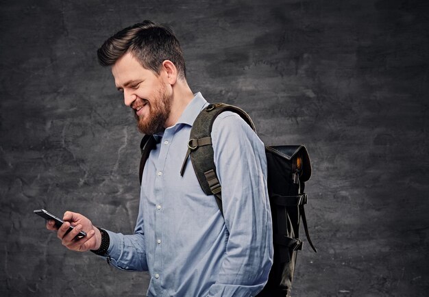 Portrait d'homme voyageur urbain barbu avec un sac à dos sur le dos à la piste GPs avec un téléphone intelligent.