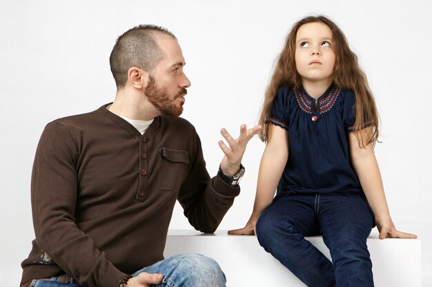 Portrait horizontal du jeune homme barbu à la mode ayant une conversation sérieuse avec sa fille gâtée coquine, lui parlant de règles.