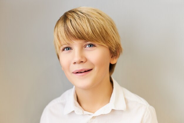 Portrait horizontal d'un écolier caucasien attrayant aux yeux bleus avec une coiffure élégante souriant joyeusement après avoir ravi l'expression du visage excité, fasciné par quelque chose d'étonnant. Émotions positives