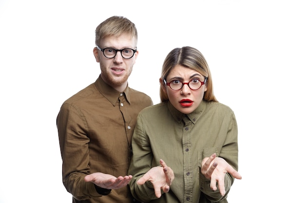 Portrait horizontal de jeune homme de race blanche désemparé et femme faisant des gestes confus tout en posant ensemble, étant perdu pour les mots, à la recherche d'indignation et d'irritation