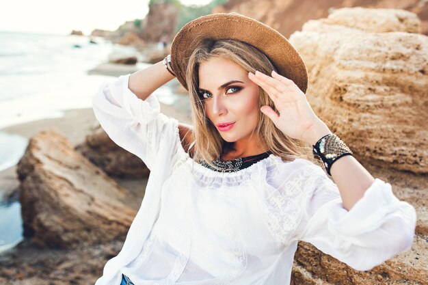 Portrait horizontal de jolie fille blonde aux cheveux longs posant à la caméra sur la plage déserte. Elle regarde la caméra.