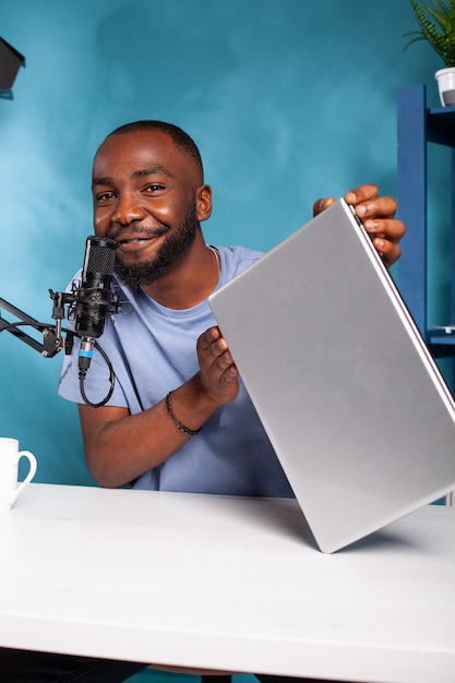 Portrait d'un influenceur afro-américain hébergeant un cadeau en direct pour la célèbre marque d'ordinateurs portables parlant dans un microphone. Créateur de contenu enregistrant un concours d'ordinateurs portables pour un podcast vidéo sur les réseaux sociaux.