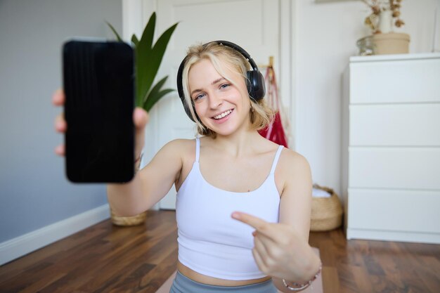 Photo gratuite portrait d'une instructrice de fitness souriante et en bonne santé à la maison montrant du doigt et la montrant