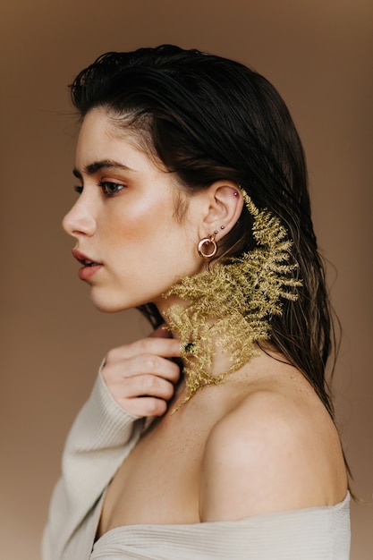 Portrait intérieur de femme brune adorable avec plante. Belle jeune femme aux cheveux noirs tenant une fleur.