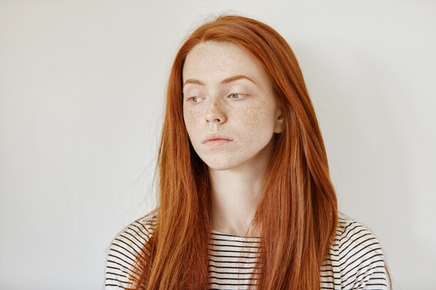 Portrait intérieur de jeune femme triste portant ses longs cheveux roux lâche regardant vers le bas avec une expression de visage malheureux