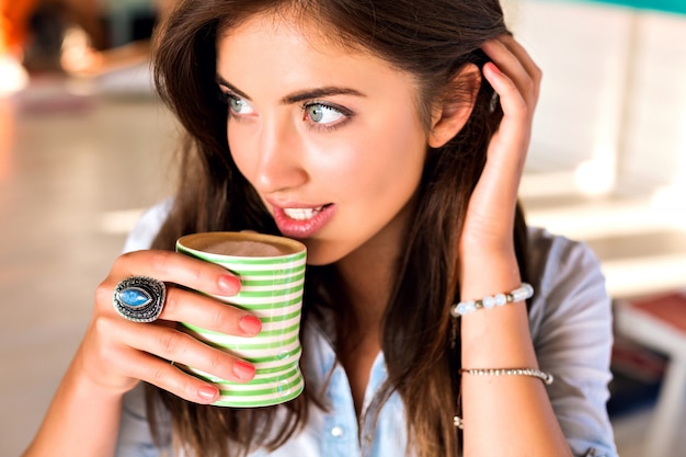Portrait d'intérieur de mode de vie de jeune femme brune posant à la cafétéria de la ville profiter de son délicieux café chaud du matin