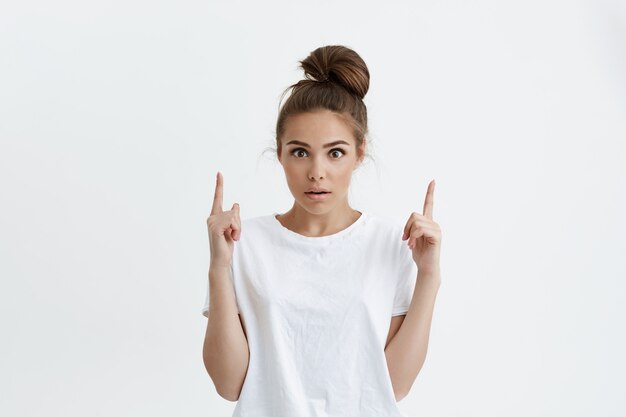 Portrait d'intérieur d'un modèle féminin mignon étonné ou choqué pointant vers le haut avec l'index,