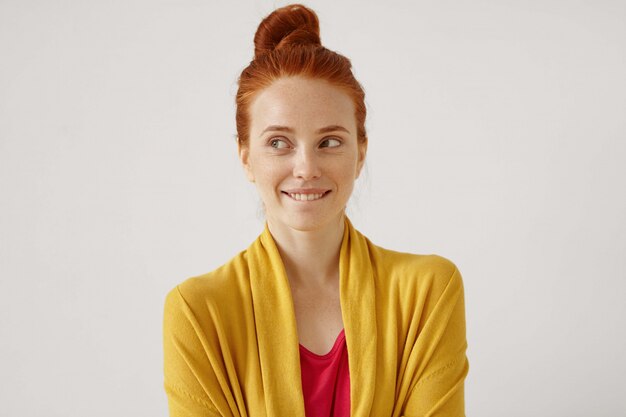 Portrait intérieur de mystérieuse charmante jeune femme gimger européenne avec noeud de cheveux à côté avec sourire énigmatique