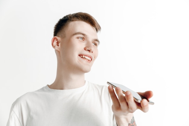 Portrait intérieur de séduisant jeune homme isolé sur fond gris, tenant le smartphone, à l'aide de la commande vocale, se sentir heureux et surpris. Émotions humaines, concept d'expression faciale.