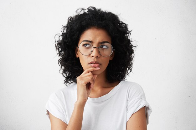 Portrait isolé de l'élégante jeune femme métisse avec des cheveux hirsutes foncés touchant son menton