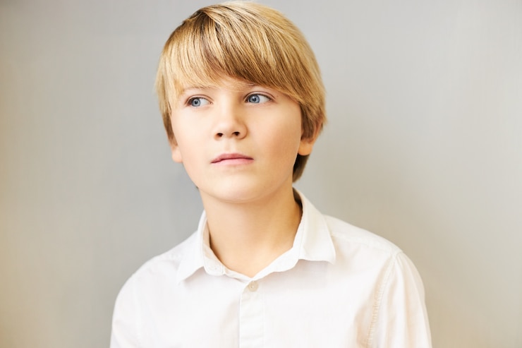 Photo gratuit portrait isolé d'un garçon caucasien étonné avec des franges et des yeux bleus à la recherche de suite avec une expression pensive mystérieuse, profondément dans ses pensées, réfléchissant, ayant une idée ou faisant un plan, posant au mur blanc