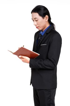 Portrait isolé d'un homme d'affaires asiatique heureux et confiant avec des cheveux longs en queue de cheval en costume d'affaires noir formel se tenant souriant tenant un ordinateur portable écrivant une note de travail importante sur fond blanc.