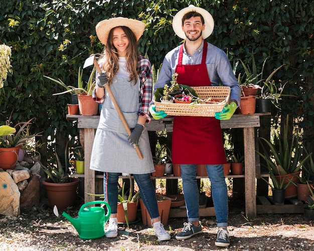 Portrait de jardinier homme et femme tenant des outils et un panier dans le jardin