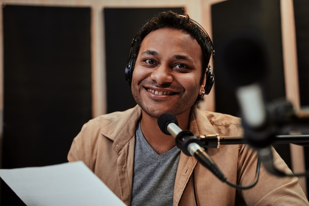 Portrait d'un jeune animateur de radio heureux dans des écouteurs souriant à la caméra tout en parlant de radiodiffusion
