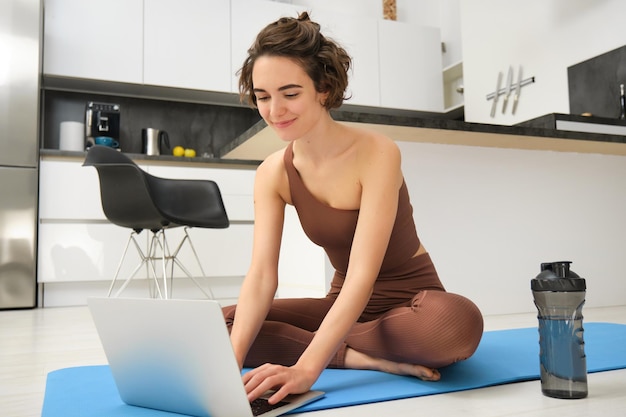 Portrait d'une jeune athlète féminine instructrice de conditionnement physique commençant un cours de gym en ligne depuis sa maison assise